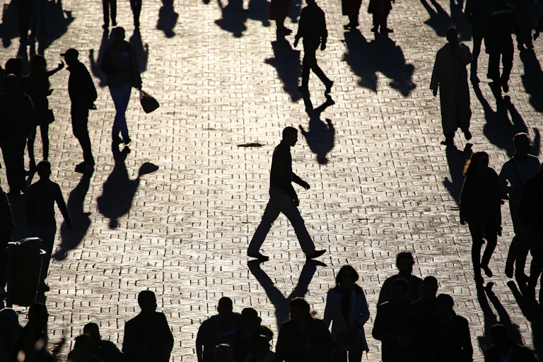 A man walks alone, apart from the crowd, on a busy plaza.
