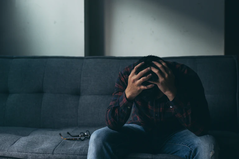 A man sits on a couch with his head in his hands