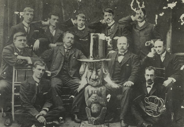 Men in suits sit around a strange statue