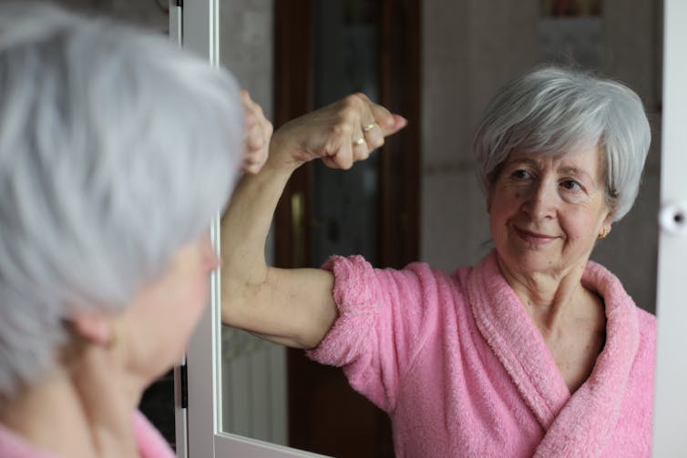 Mulher idosa flexionando bíceps no espelho