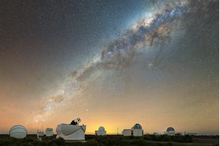 Telescopes and satellite dishes are seen beneath a vividly starry sky