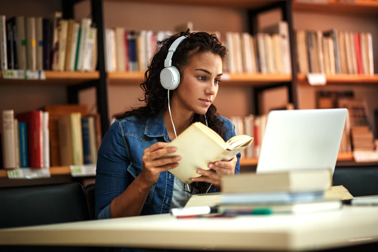 A student sits in a library with headphones on.