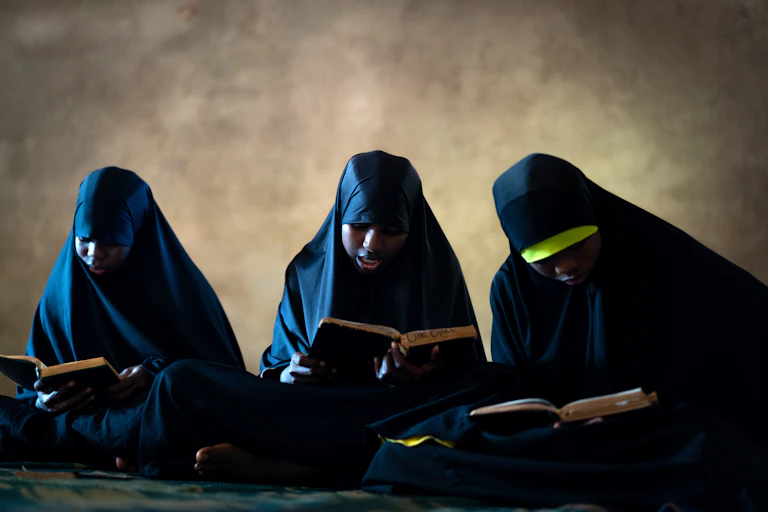 Veiled girls sit on the floor with books in their hands.