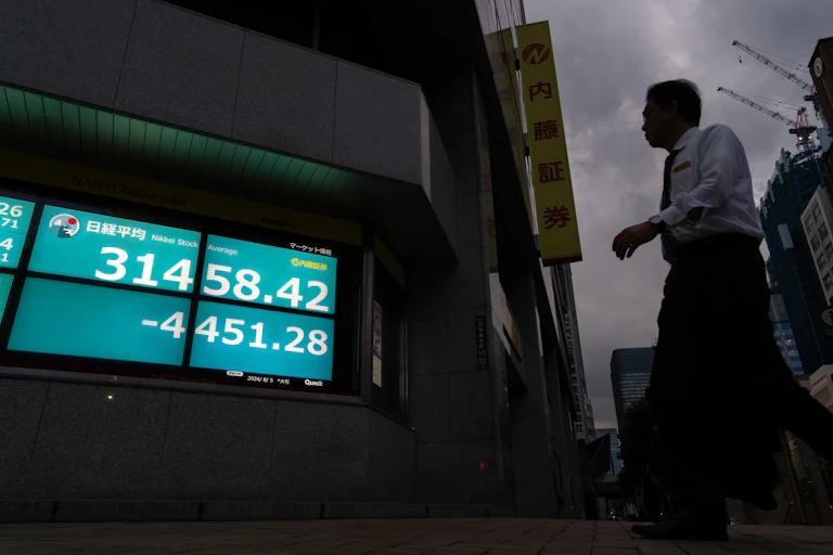 A man walks in front of a digital screen showing falling numbers. Behind him is a gloomy sky.