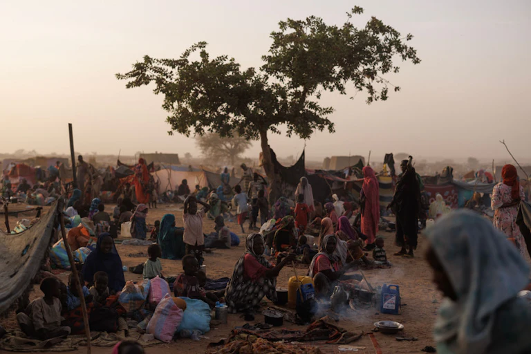 A group of women and children sitting on the ground with makeshift tents scattered among them