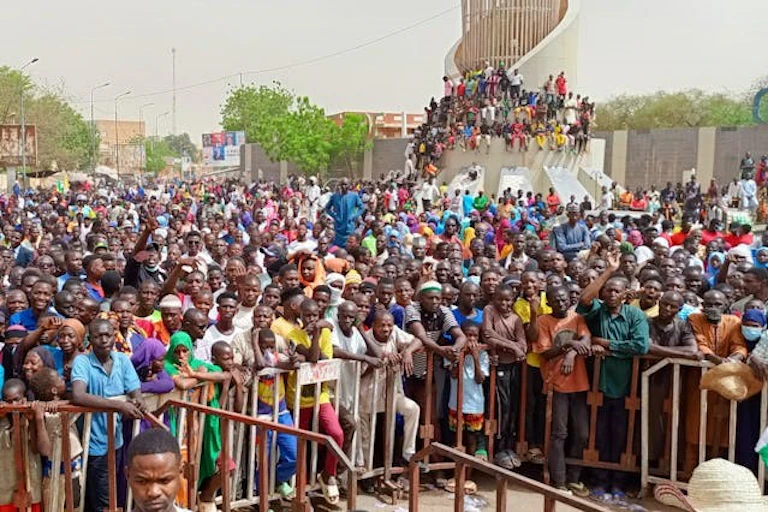 Foule de personnes en plein air, contre des barrières métalliques
