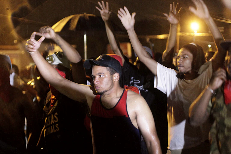 A group of Black people are raising their arms to protest the police shooting of an unarmed Black teenager.