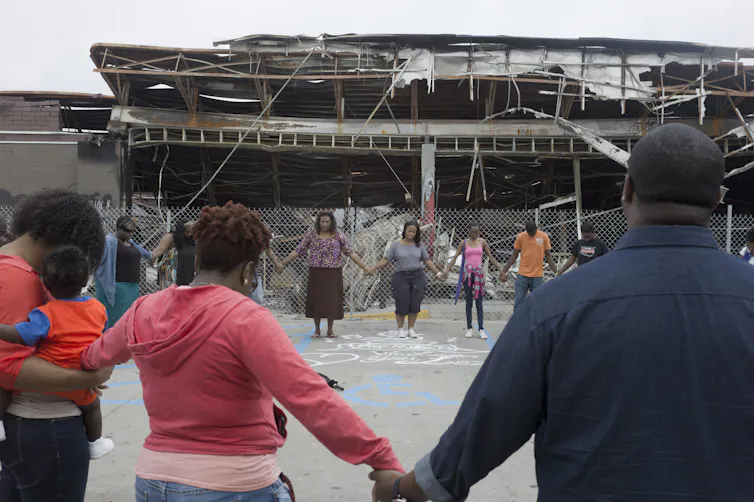 A group of Black people are holding hands while standing in a circle.