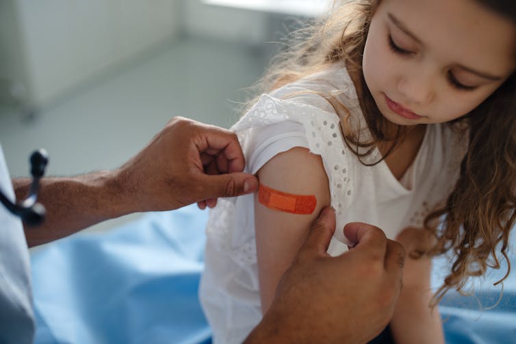A doctor placing a band-aid onto a girl's arm after a vaccination.