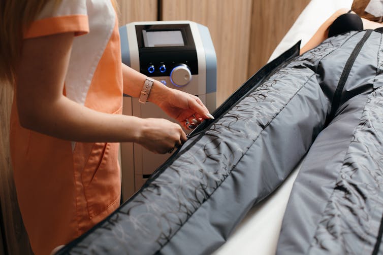 therapist adjusts device with inflated pants on person's legs