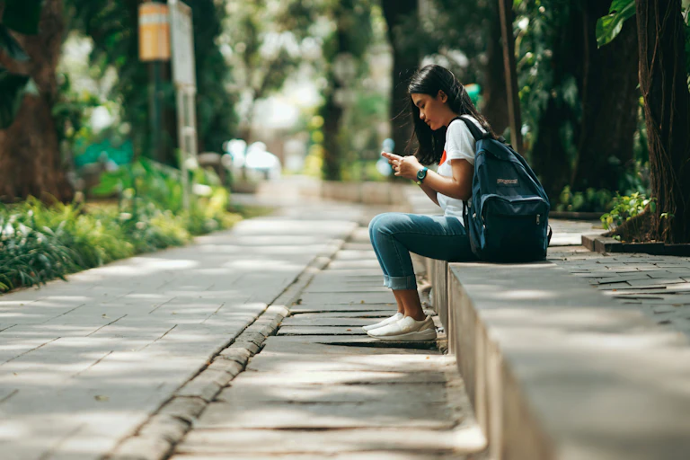 Girl sits waiting for a bus, looking at her phone