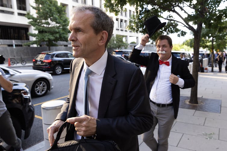 Suited lawyer walks in front of an activist dressed as the Monopoly man
