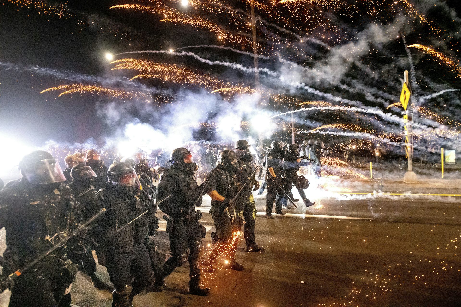 Plumes of smoke fly towards a crowd of protesters at night.