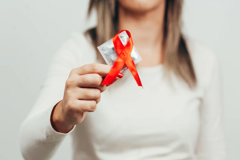Woman holding a red ribbon and a condom