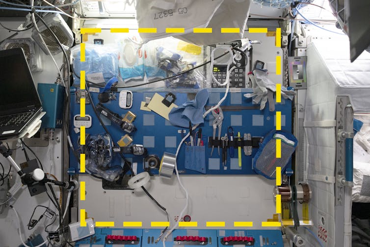 A wall of a module with a blue metal panel and many Velcro patches. There is a superimposed square made of a yellow dotted line.