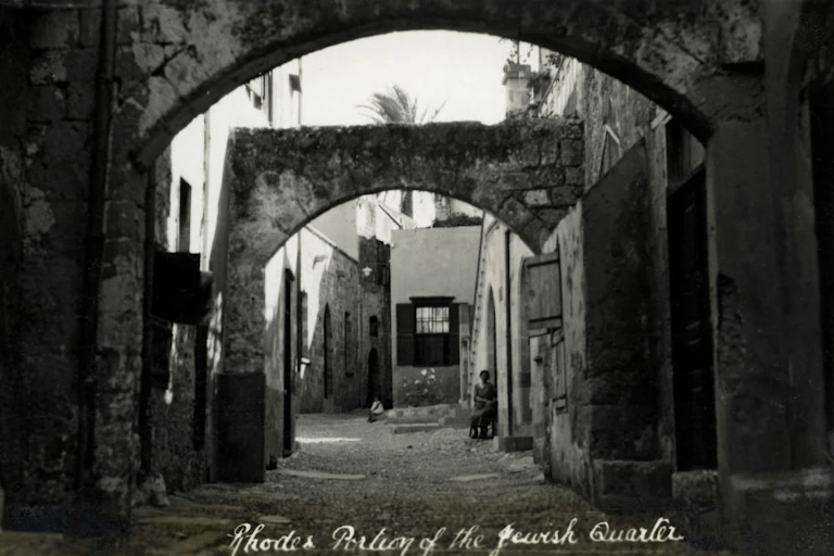 A black and white photograph of stone archways in a narrow street.