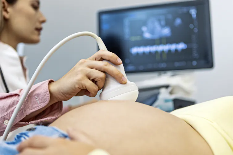 Um médico realiza um ultrassom em uma pessoa grávida.