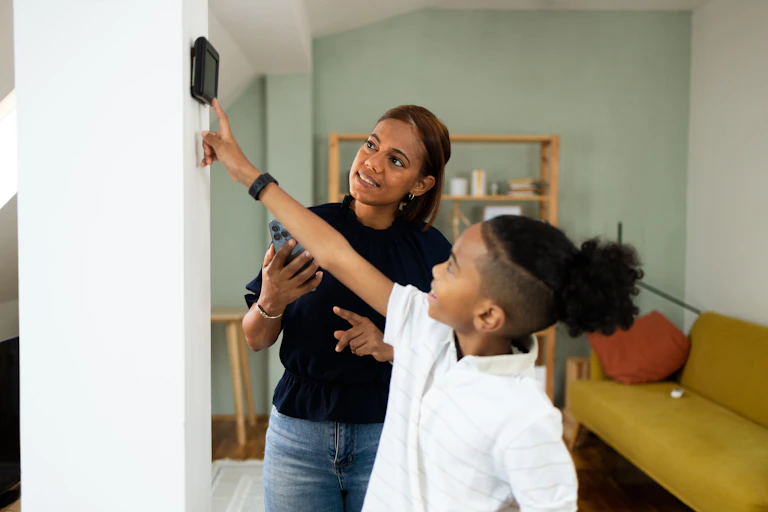 a boy points to a small display screen mounted on a post as a woman looks at the screen