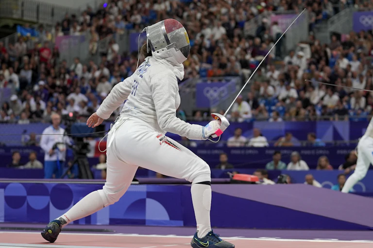 A fencer lunges foward toward their opponent, who is off-screen