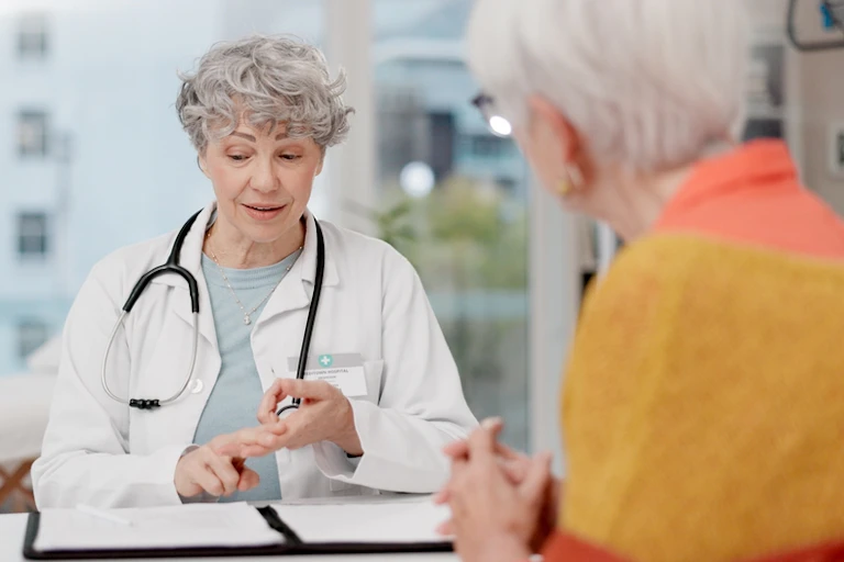 Older female doctor with white coat and stethoscope consulting with older female patient