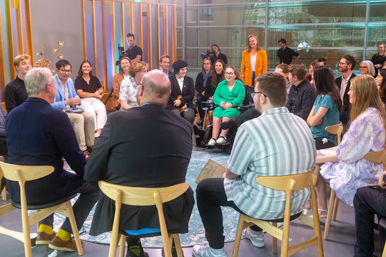 group of people on chairs and standing in circles with television cameras set up