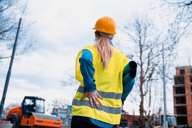 Female construction worker clutching back in pain on worksite on cloudy day