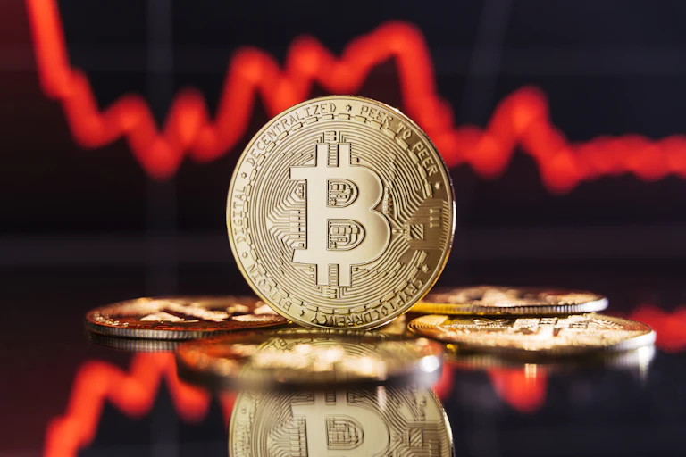 Graphic of a bitcoin in front of a red downward-trending stock graph