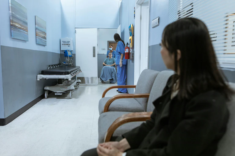 Woman sits on chair looking along hospital corridor