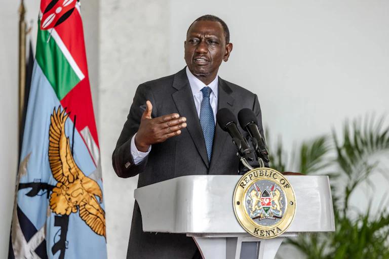 A man standing at a podium written 'Republic of Kenya' and speaking into two microphones in front of him