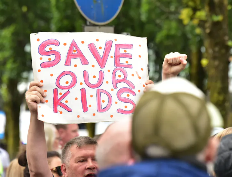 A man holding up a 'save our kids' poster at a protest