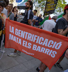 A crowd of tourism protesters in Barcelona with an orange banner that reads 'Gentrification kills neighbourhoods'.