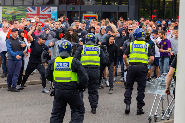 A group of men rioting with three policemen in the foreground.