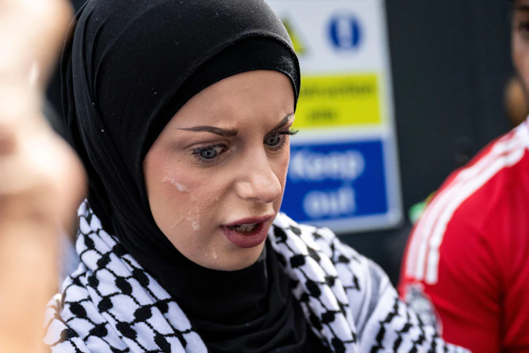 A woman wearing a headscarf looking shocked, with spit on her face.