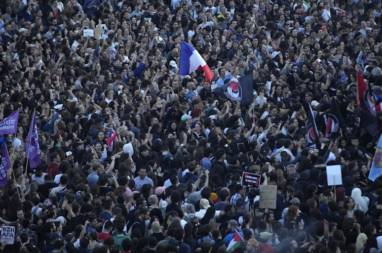 A sea of people in a city square, one waving a large blue, white and red flag.