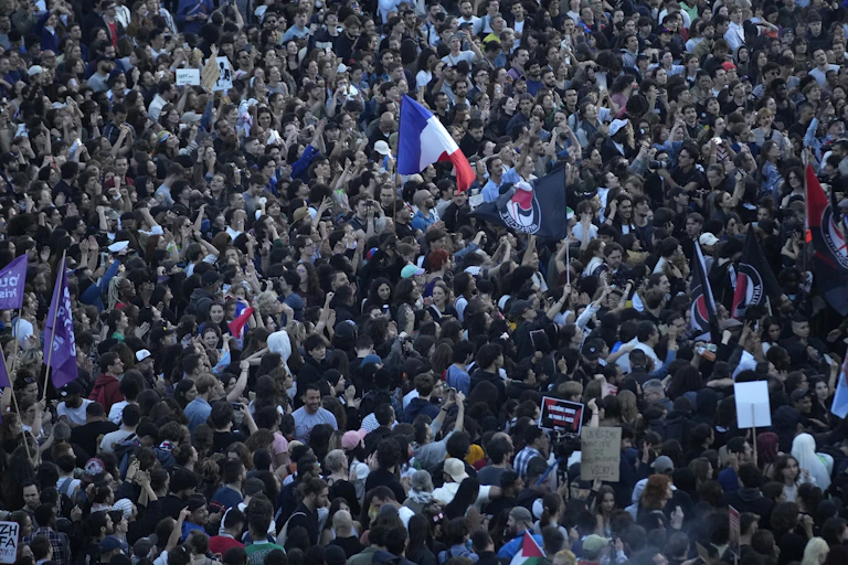 A sea of people in a city square, one waving a large blue, white and red flag.