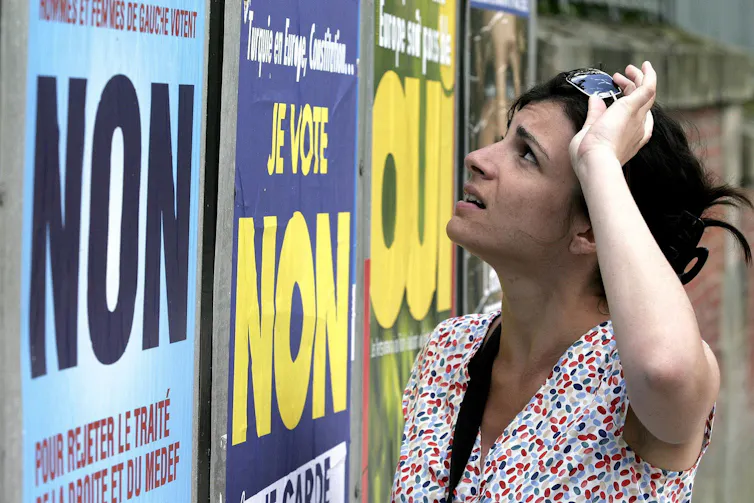A woman with short dark hair looks at political posters.