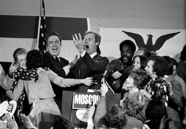A man throws his hand up in relief as people celebrate around him.