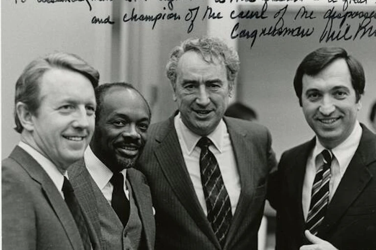Four men in suits and ties, smiling for the camera in a photo inscribed from one of them to another.