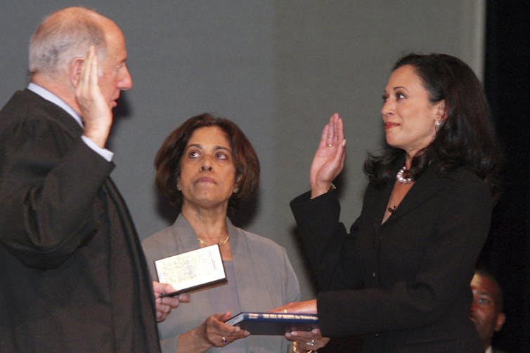 A woman with dark brown hair in a dark jacket swears an oath with her right hand raised.