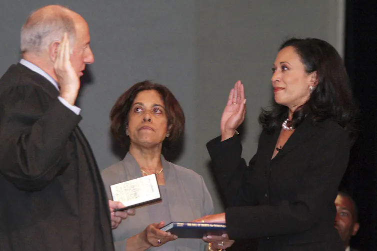 A woman with dark brown hair in a dark jacket swears an oath with her right hand raised.