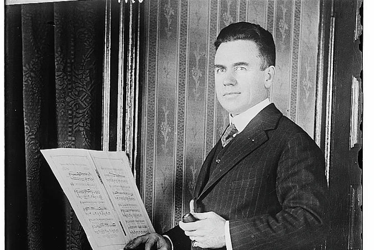 black and white photo of a man in a suit standing in front of sheet music on a stand