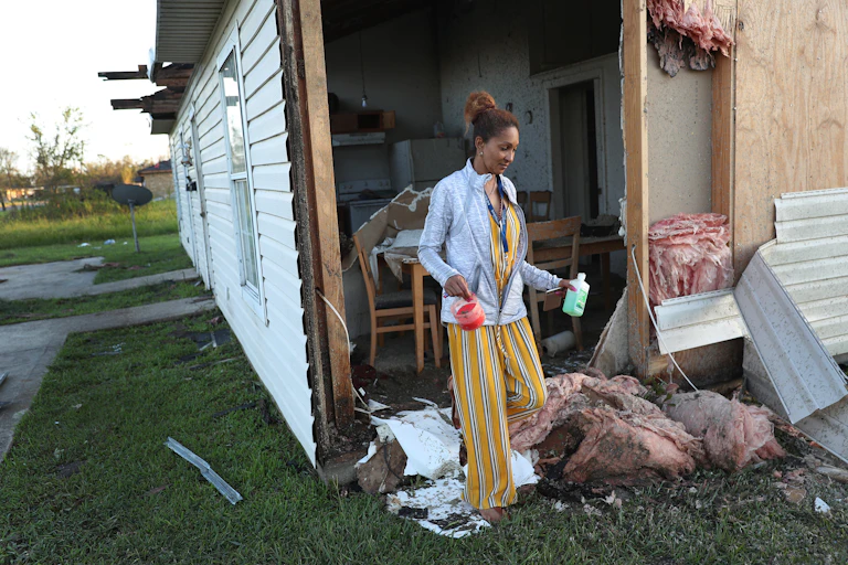 A woman steps through what was once a wall from her kitchen to her yard after a hurricane.