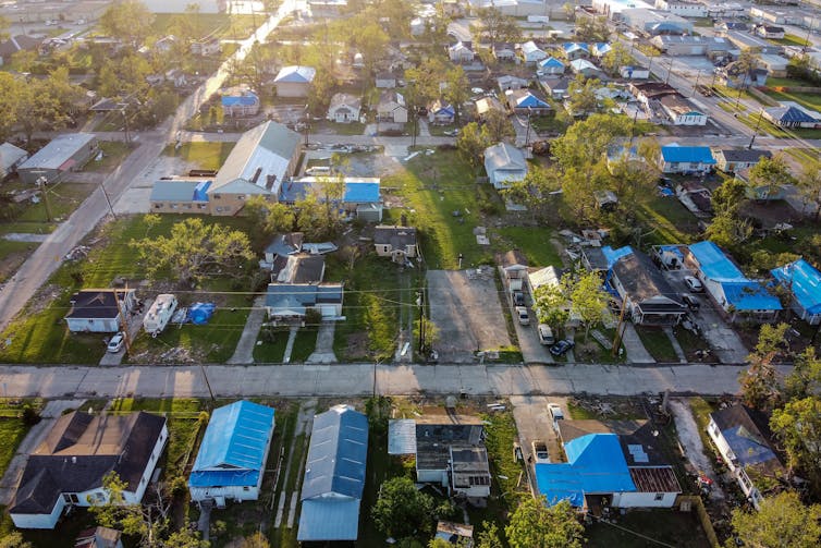 An aerial view of a neighborhood with most of the homes' roofs either missing or covered with a blue tarp.