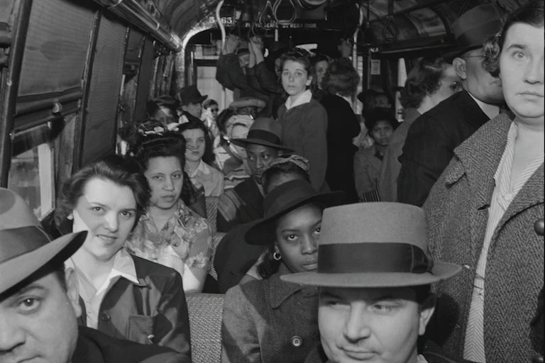 A crowded streetcar with riders seated and standing, in hats and coats