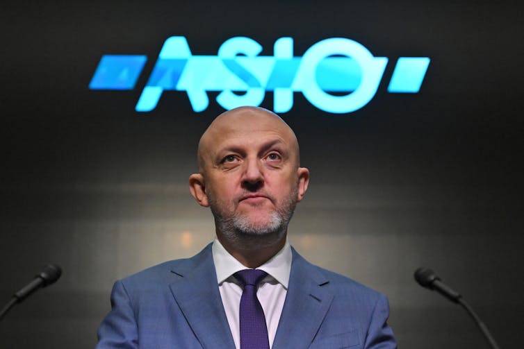 A man in a suit stands in front of a logo saying ASIO