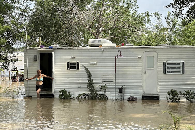 A woman walks out of mobile home surrounded by muddy flood water knee-deep.