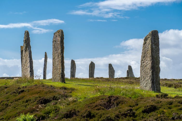 A circle of upright irregular stones on a hilltop under a blue sky.