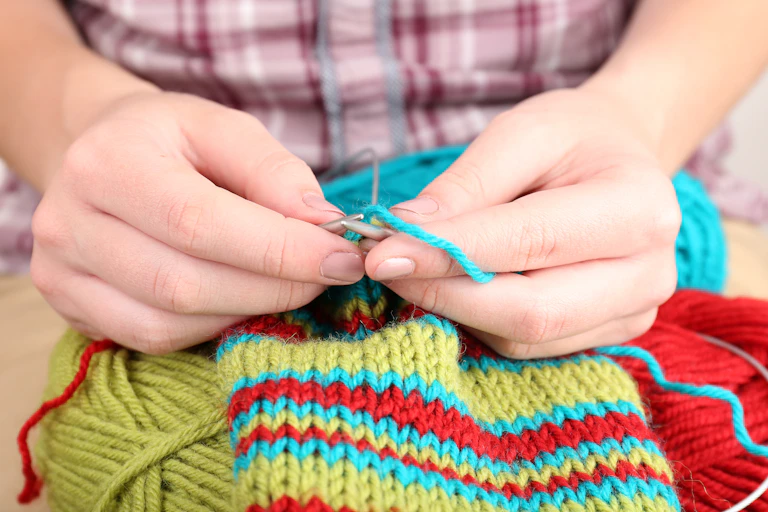 Hands knit with bright-coloured wool.