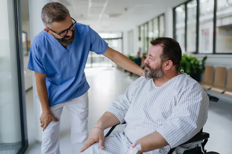 A health-care worker talks to a patient in a wheelchair in a hospital.