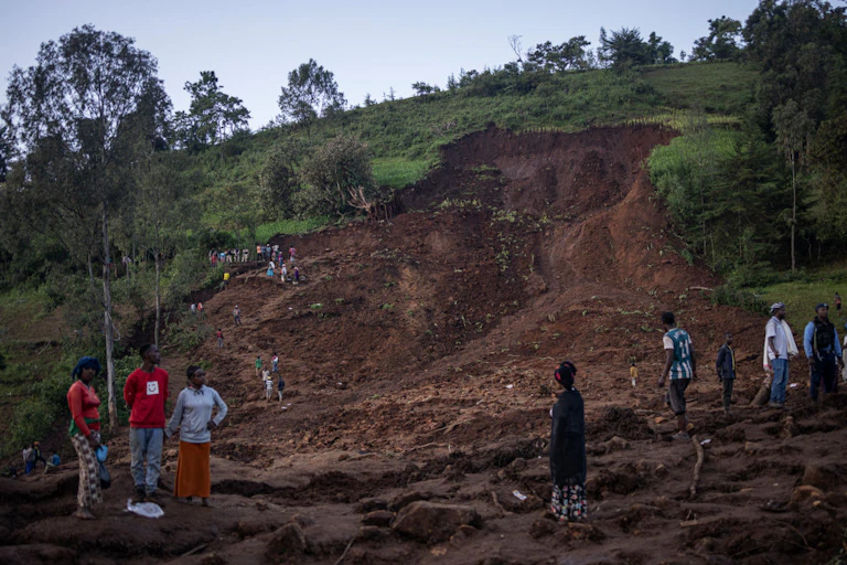 People stand on a column of red earth which peeled off a hillside above burying some people alive.